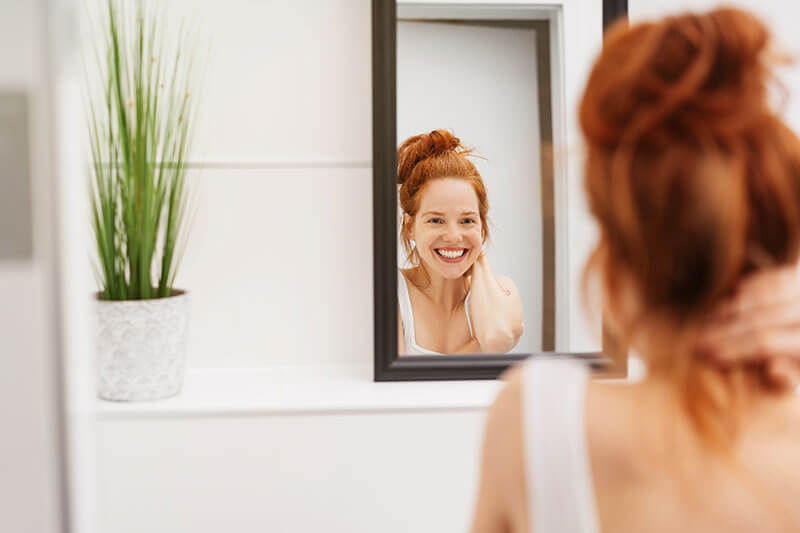young woman smiling and looking in the mirror